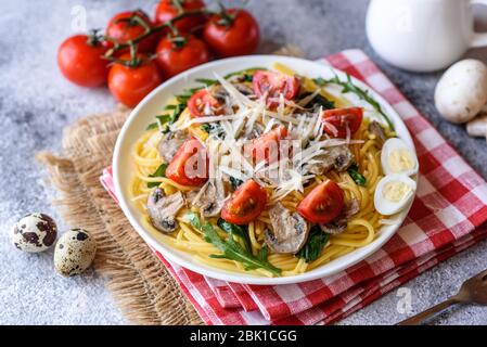 Spaghetti con funghi, formaggio, spinaci, rukkola e pomodori ciliegini. Piatti italiani, cultura mediterranea Foto Stock