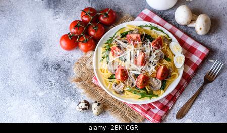 Spaghetti con funghi, formaggio, spinaci, rukkola e pomodori ciliegini. Piatti italiani, cultura mediterranea Foto Stock