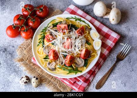 Spaghetti con funghi, formaggio, spinaci, rukkola e pomodori ciliegini. Piatti italiani, cultura mediterranea Foto Stock