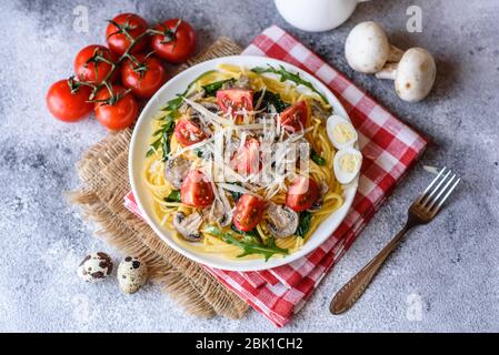 Spaghetti con funghi, formaggio, spinaci, rukkola e pomodori ciliegini. Piatti italiani, cultura mediterranea Foto Stock