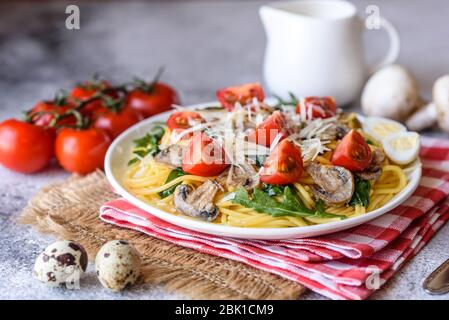 Spaghetti con funghi, formaggio, spinaci, rukkola e pomodori ciliegini. Piatti italiani, cultura mediterranea Foto Stock