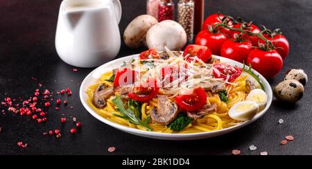 Spaghetti con funghi, formaggio, spinaci, rukkola e pomodori ciliegini. Piatti italiani, cultura mediterranea Foto Stock