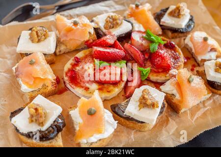 Varietà di pane tostato con: Filetto di salmone affumicato e formaggio cremoso; melanzana marinata con noci e formaggio di capra alla griglia e fragola Foto Stock