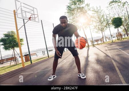 Attività all'aperto. L'uomo africano che gioca a basket sul campo dribbling concentrato Foto Stock