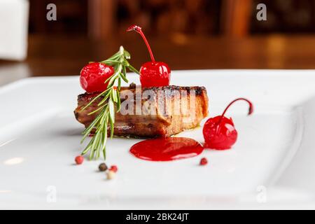 Costolette di maiale alla griglia decorate con rosmarino e ciliegia caramellate servite su un piatto bianco in un ristorante Foto Stock