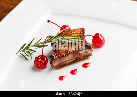 Costolette di maiale alla griglia decorate con rosmarino e ciliegia caramellate servite su un piatto bianco in un ristorante Foto Stock