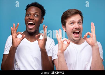 Due uomini felici afro-americani e caucasici che mostrano un gesto ok. Scatto studio Foto Stock