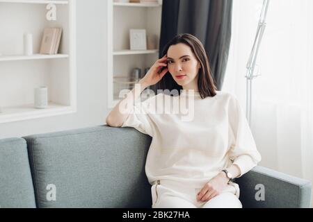 Bella donna elegante in bianco rilassante sul divano. Foto Stock