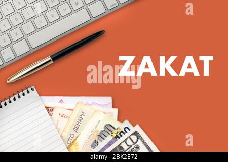 TESTO ZAKAT (tassa islamica) con blocco note, tastiera, banconota multipla o valuta e penna stilografica su sfondo arancione. Zakat (tassa islamica), Business and Foto Stock