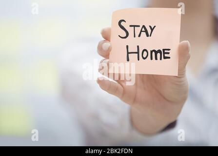 Mani che tengono un'annotazione adesiva con il testo di soggiorno a casa Foto Stock