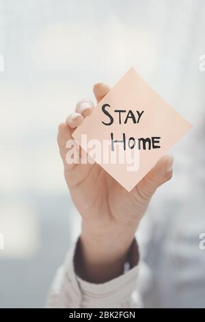 Mano che tiene nota adesiva con il testo di soggiorno a casa Foto Stock