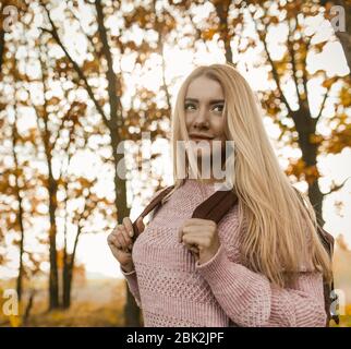 Affascinante passeggiata in stile biondo con zaino nella foresta d'autunno Foto Stock