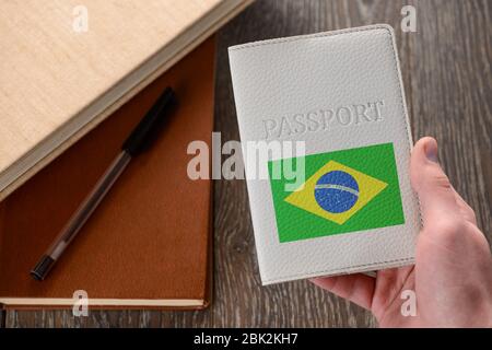 Mano con passaporto brasiliano. Libri in background Foto Stock