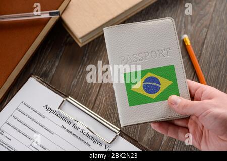 Mano con passaporto brasiliano, modulo di richiesta in background Foto Stock