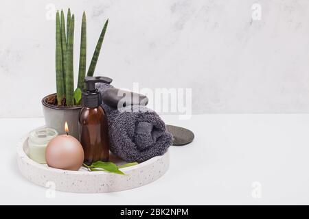 Composizione Spa, prodotti per la cura del corpo, asciugamano e candela su vassoio bianco Foto Stock