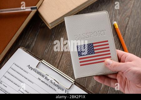 Mano con passaporto con bandiera USA, modulo di richiesta in background Foto Stock