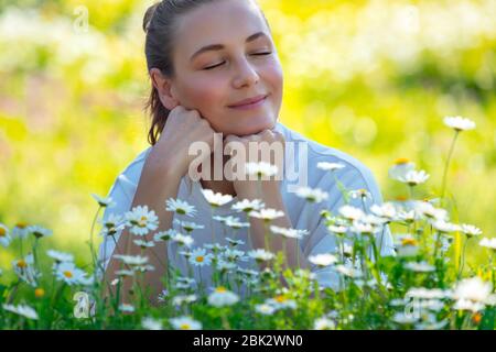 Giovane donna con occhi chiusi adagiata sull'erba fresca verde tra i piccoli e dolci fiori di margherita, godendo della bellezza e della freschezza della natura primaverile