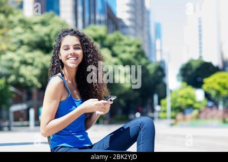 Giovane donna ridente adulta inviare messaggio con il telefono in città in estate Foto Stock