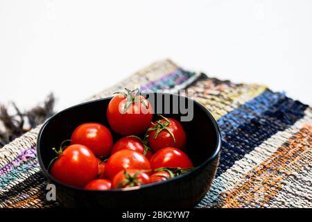 Dettaglio di pomodori ciliegini maturi in una piccola ciotola nera su un tovagliolo rustico. Ingredienti e concetto di cibo Foto Stock