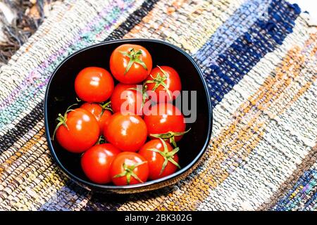 Dettaglio di pomodori ciliegini maturi in una piccola ciotola nera su un tovagliolo rustico. Ingredienti e concetto di cibo Foto Stock