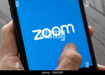 Telefono con una mano che mostra l'app Zoom Cloud Meetings. Lavoro e riunioni da casa con uno smartphone. Foto Stock