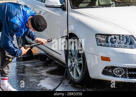 Lavatrice professionale in uniforme casual lavaggio auto di lusso con pistola ad acqua su un lavaggio auto all'aperto Foto Stock