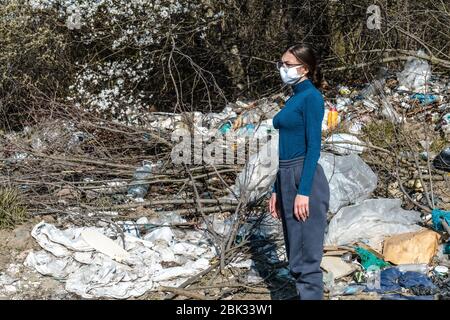 La ragazza bruna triste in occhiali si trova vicino al cestino che giace tra la foresta Foto Stock