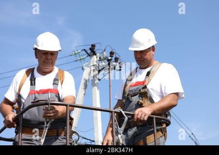 Due lavoratori elettrici su un ascensore. Gli ingegneri si alzano su una gru per riparare un supporto alto. Gli uomini eliminano l'incidente alla stazione di alta quota Foto Stock