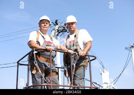 Due lavoratori elettrici su un ascensore. Gli ingegneri si alzano su una gru per riparare un supporto alto. Gli uomini eliminano l'incidente alla stazione di alta quota Foto Stock