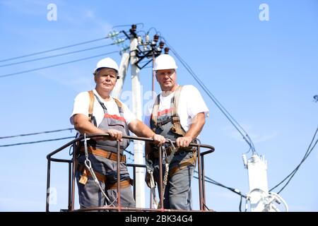 Due lavoratori elettrici su un ascensore. Gli ingegneri si alzano su una gru per riparare un supporto alto. Gli uomini eliminano l'incidente alla stazione di alta quota Foto Stock