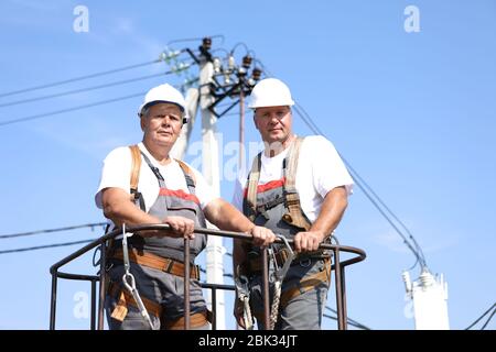 Due lavoratori elettrici su un ascensore. Gli ingegneri si alzano su una gru per riparare un supporto alto. Gli uomini eliminano l'incidente alla stazione di alta quota Foto Stock