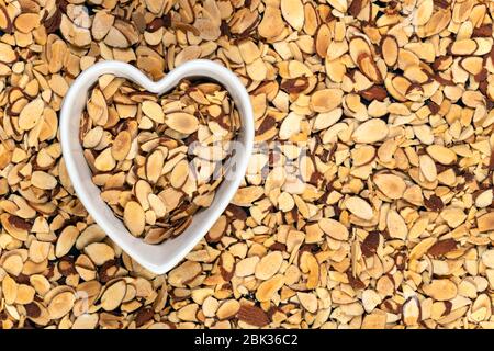 Pile di mandorle a fette arrosto in una ciotola a forma di cuore. Foto Stock