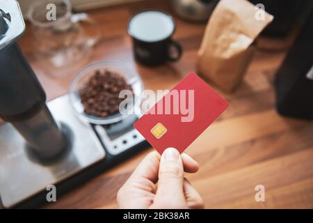 Uomo che detiene una carta di debito rossa vuota un bar che paga per un take out. Foto Stock