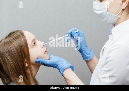 Pediatra che preleva il campione di test del muco nasale dal naso della ragazza di età elementare che esegue la procedura di test del virus respiratorio Foto Stock