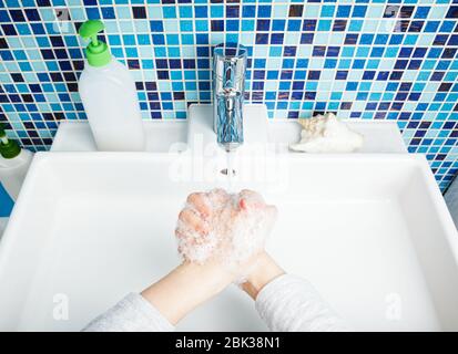 Il bambino lava diligentemente le mani con sapone antibatterico e acqua eseguendo le misure protettive di base contro la diffusione di deseas COVID-19 di coronavirus Foto Stock