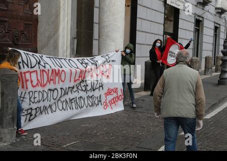 Un uomo passa accanto ai militanti di Potere al Popolo (potere al popolo) movimento indossando maschere protettive tenere una bandiera che scrive 'tutto andrà bene se difenderemo i lavoratori, Per lo stipendio di emergenza' per protestare alla Festa del lavoro a causa della perdita di posti di lavoro dovuta alla quarantena che chiede maggiori sovvenzioni a sostegno del reddito durante la chiusura a causa del decreto governativo che dichiara tutta l'Italia un'area protetta per combattere l'infezione da Covid-19 - Coronavirus. Un nuovo decreto governativo ha stabilito regole per riaprire gradualmente le attività economiche e sociali come ristoranti. Foto Stock