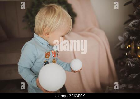 Un ragazzino biondo con una palla di Natale tra le mani sta studiando il mondo intorno a lui. Foto Stock