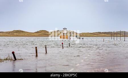 La strada alberata sull'isola di Lindisfarne con la scatola del rifugio di emergenza e i segnalatori stradali, Northumberland, Inghilterra Foto Stock