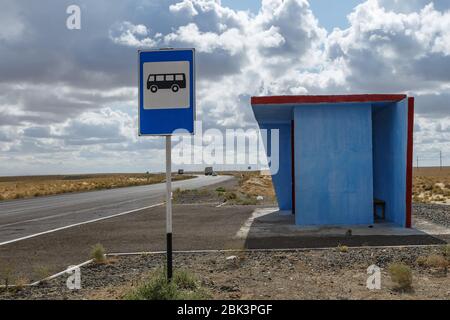 Fermata blu dell'autobus e un cartello di fermata su un pilastro nella steppa del Kazakistan. Foto Stock