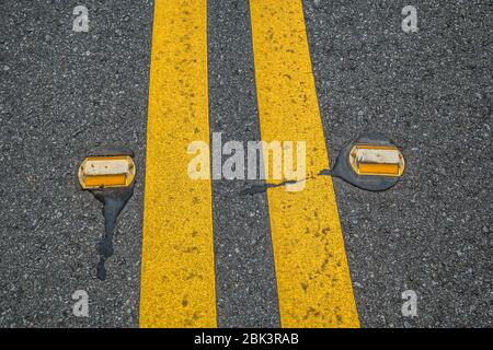 Una doppia linea gialla sulla strada con riflettori di corsia su entrambi i lati per vedere di notte per rimanere in corsia Foto Stock