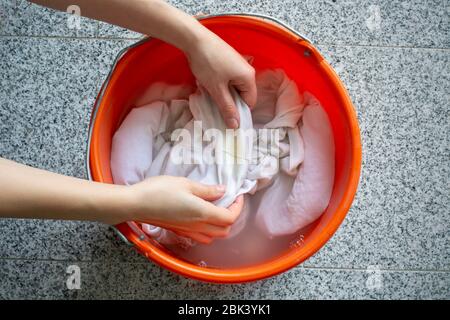 Pulizia manuale del bucato. Le mani delle donne lavano le camicie bianche sporche con le macchie gialle del sudore per impregnarlo in un secchio Foto Stock