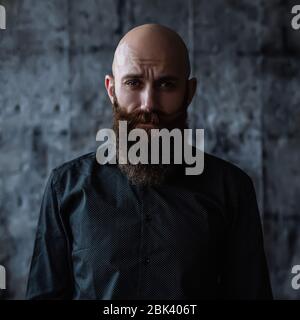 Ritratto di un bell'uomo bearded audace di mezza età in camicia nera su sfondo scuro Foto Stock