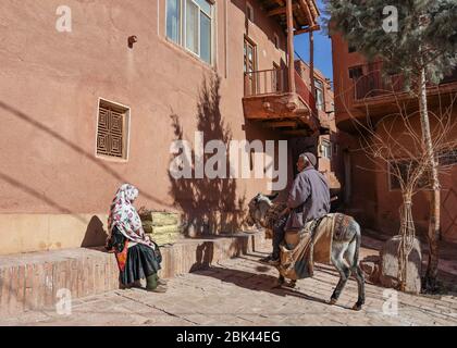 Vecchio uomo seduto su asino che parla con una donna vestito in abiti tradizionali nel villaggio di Abyaneh, provincia di Esfahan, Iran, Persia, Medio Oriente Foto Stock