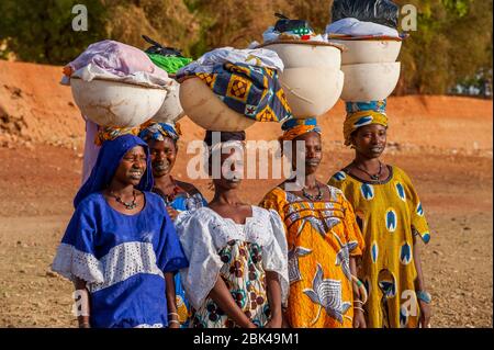 Donne locali che camminano e trasportano la lavanderia sulla loro testa sulla riva del fiume Bani a Mopti in Mali, Africa occidentale. Foto Stock