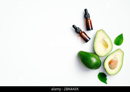 Olio essenziale naturale e avocado fresco maturo su sfondo bianco. Disposizione piatta, vista dall'alto. Idratante organico per capelli, viso e pelle, olio per massaggi Foto Stock