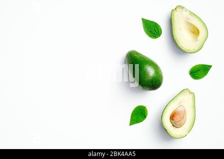 Avocado a fette mature con foglie verdi su sfondo bianco. Disposizione piatta, vista dall'alto, spazio per la copia. Foto Stock