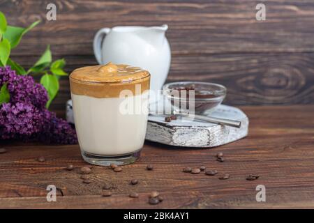 Il caffè Dalgona è una bevanda coreana fredda alla moda. Caffè gustoso e aromatico con latte e zucchero in un bicchiere su fondo di legno. Spazio di copia Foto Stock