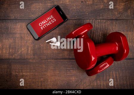 Manubri rossi e smartphone su sfondo boschivo. App per la formazione in ambienti chiusi. Programma Fitness online. Allenamento online a casa. Vista dall'alto, Covid-19 Coronavi Foto Stock