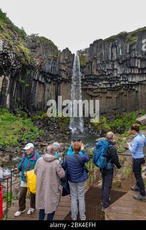 I visitatori si trovano di fronte alla cascata delle cascate Svartifoss (Black Falls), al Parco Nazionale Vatnajökull, nell'Islanda meridionale. Foto Stock
