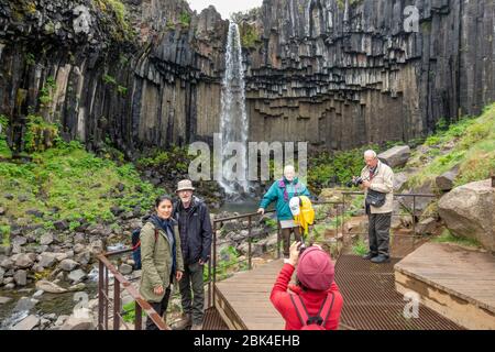 I visitatori si trovano di fronte alla cascata delle cascate Svartifoss (Black Falls), al Parco Nazionale Vatnajökull, nell'Islanda meridionale. Foto Stock